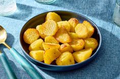 a blue bowl filled with fried potatoes next to two spoons on a tablecloth