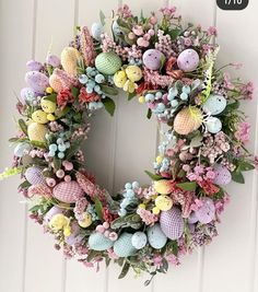 an easter wreath is hanging on the front door with eggs, flowers and leaves in pastel colors