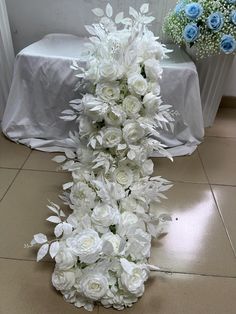 a bouquet of white flowers sitting on top of a floor next to a table covered in blue and white cloths