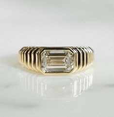 a gold ring with an emerald cut diamond in the center, on a white surface