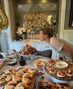 a woman standing over a table filled with plates of food and desserts on it