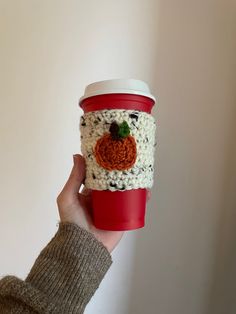 a hand holding a coffee cup with a crocheted pumpkin on the top and bottom