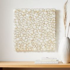 a white vase sitting on top of a wooden table next to a wall mounted art piece