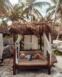 a man laying on top of a bed under a straw covered roof next to palm trees