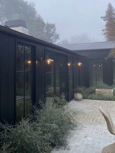 an outdoor patio area with chairs and lights on the side of it, surrounded by greenery