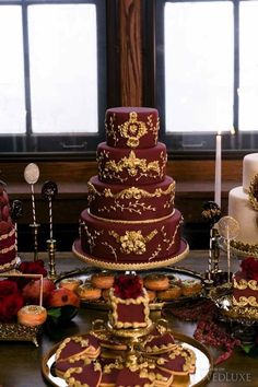 a table topped with three tiered cakes covered in red and gold frosting next to candles