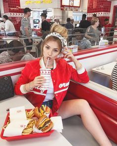 a woman sitting at a table with a tray of food in front of her while talking on the phone