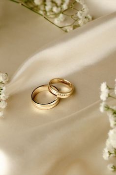 two gold wedding rings sitting on top of a white cloth next to some baby's breath flowers