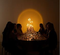 a group of people sitting around a dinner table with candles on the wall behind them