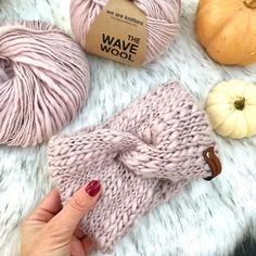 a woman's hand holding a pink knitted mitt next to some pumpkins