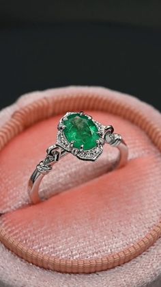 an emerald and diamond ring sitting on top of a pink velvet cushion in a box