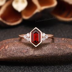 a close up of a red stone ring on top of a piece of wood with flowers in the background