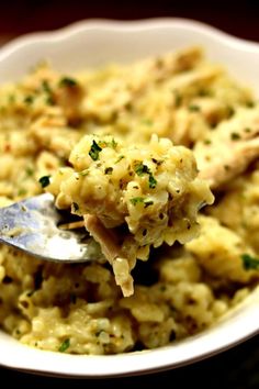 a spoon full of macaroni and cheese with parsley on top, in a white bowl