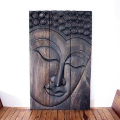 a wooden wall hanging with a buddha head on it's face in front of a white wall