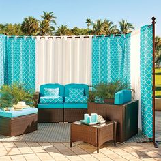 an outdoor living area with blue and white curtains, wicker furniture and potted plants