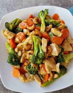 a white plate topped with chicken, broccoli and carrots next to a blue napkin