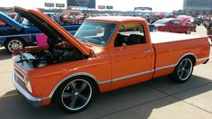 an orange pickup truck parked in a parking lot with other cars and trucks behind it