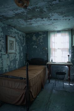 a bed in a room with peeling paint on the walls and ceiling, next to a window