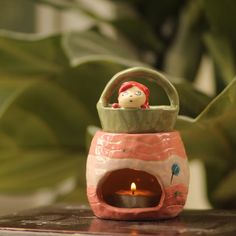 a candle holder with a doll in it on a table next to a potted plant