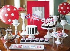 a table topped with cupcakes and cakes covered in british flag frosting next to balloons