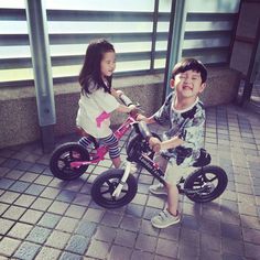 two young children riding bikes in front of a building