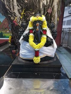 a statue of lord ganesh in front of a tree with yellow and red flowers