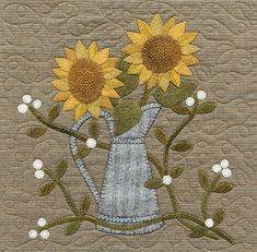 two sunflowers in a vase on a quilt