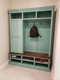 a green bench with shoes on it and a backpack hanging from the wall behind it