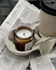 a coffee cup sitting on top of a newspaper next to a candle