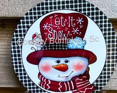 a snowman with a red hat and scarf on it's head is hanging from the side of a wooden wall