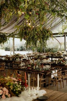 tables and chairs are set up for an outdoor wedding reception with greenery hanging from the ceiling