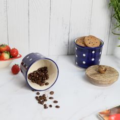 two bowls filled with coffee beans next to strawberries and other fruit on a table