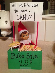 an elf is sitting behind a sign that says, all profits used to buy candy bake sale 25 cents