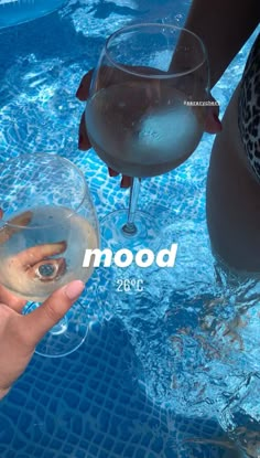 two people holding wine glasses in front of a swimming pool with the word mood on it