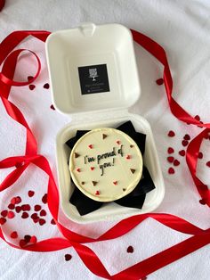 a small cake in a white box with red ribbon on the table next to it