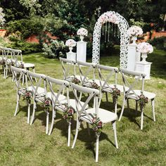 a row of white chairs sitting on top of a lush green field covered in flowers