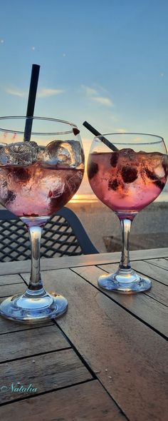 two glasses filled with drinks sitting on top of a wooden table next to each other