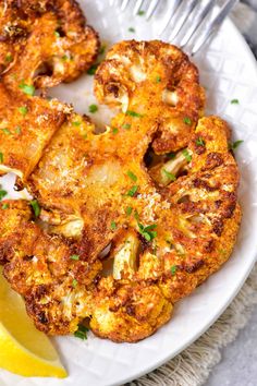 a white plate topped with fried cauliflower and lemon wedges next to a fork