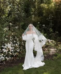 a woman in a wedding dress and veil posing for the camera with flowers behind her