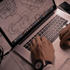 a person working on a laptop computer while sitting at a desk with blueprints