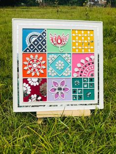 an art piece sitting in the grass on top of a wooden block with different designs