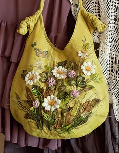 a yellow purse with flowers on it hanging from a wall next to lace doily