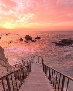 the stairs lead down to the beach as the sun sets over the water and rocks