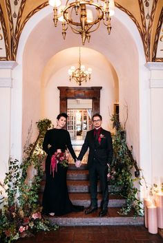 two people holding hands while standing on steps in front of a chandelier with candles