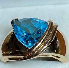 A gorgeous 10k yellow gold blue topaz solitaire ring for your consideration. This unique ring features a trillion cut blue topaz that measures 10mm x 10mm. The unique setting loops over the prong set topaz on one side. The ring is 12.2mm at its widest and tapers to 2.2mm in the back. It is a size 5 1/2 and weighs in at 4 grams. It's a great ring for any occasion! Unique Ring, Solitaire Ring, Rings Statement, Unique Rings, Prong Setting, Blue Topaz, Statement Rings, Topaz, Gemstone Rings