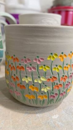 a bowl with flowers painted on it sitting on a counter next to other bowls and cups