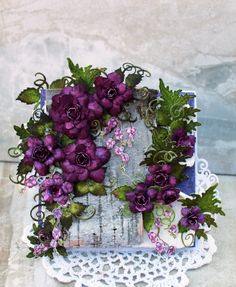 purple flowers and green leaves are arranged on a lace doily next to an old window