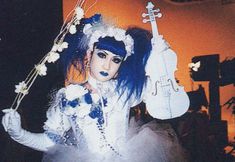 a woman with blue hair and makeup holding a violin