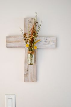 a cross mounted on the wall with flowers in a vase hanging from it's side