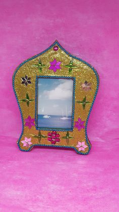 a gold frame with pink flowers and blue trim on it, against a pink background